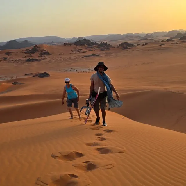 Deux voyageurs sur une crête de dune au coucher du soleil, traces de pas dans le sable