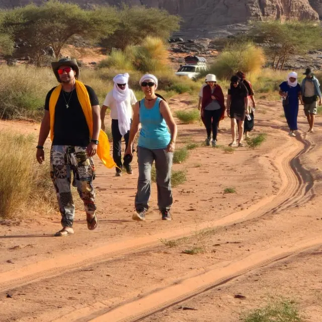 Voyageurs en marche sur une piste de sable, au pied de hautes falaises de grès