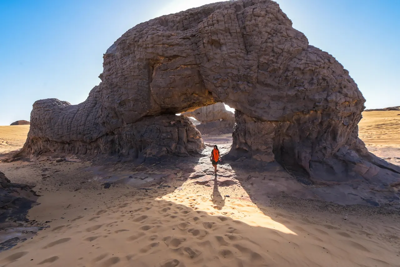 Grande arche de grès sombre au-dessus du sable, dans le Hoggar, région de Tamanrasset