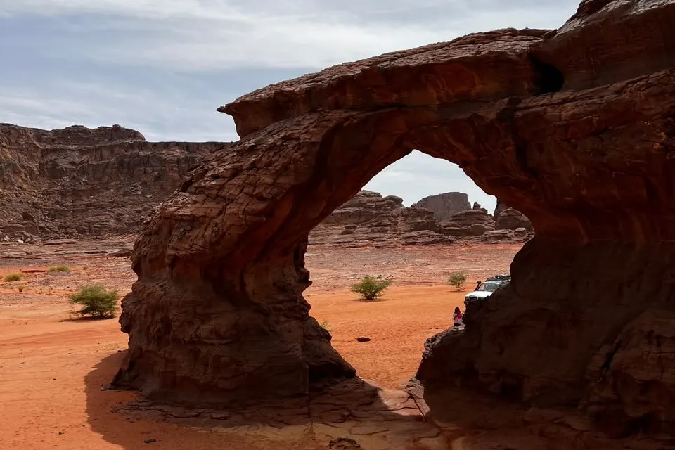 Arche de grès au milieu du sable rouge de la Tadrart, plateaux rocheux à l'horizon