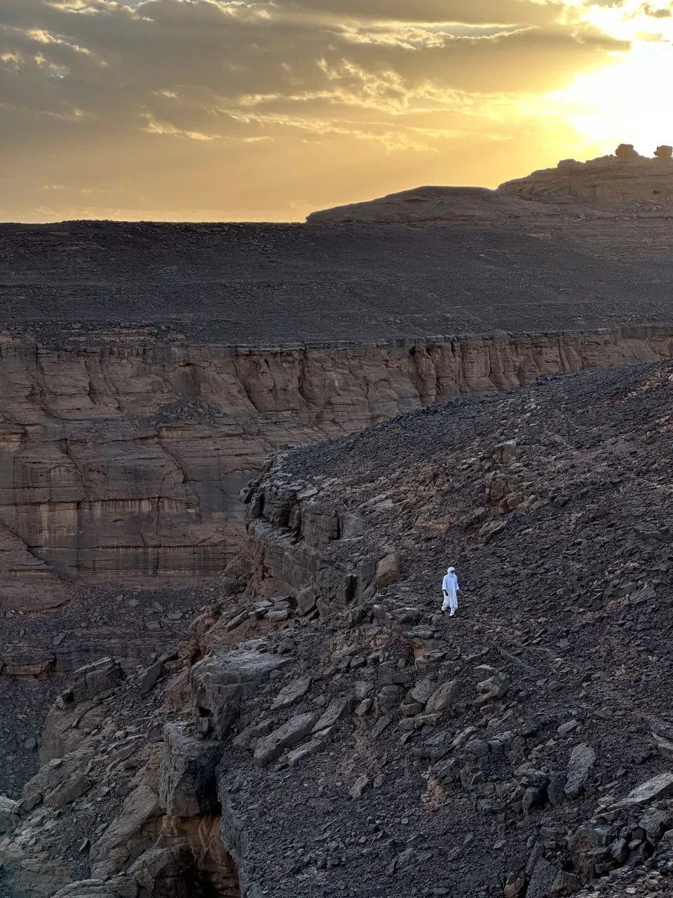 Silhouette en tenue blanche au bord d'un canyon, au coucher du soleil