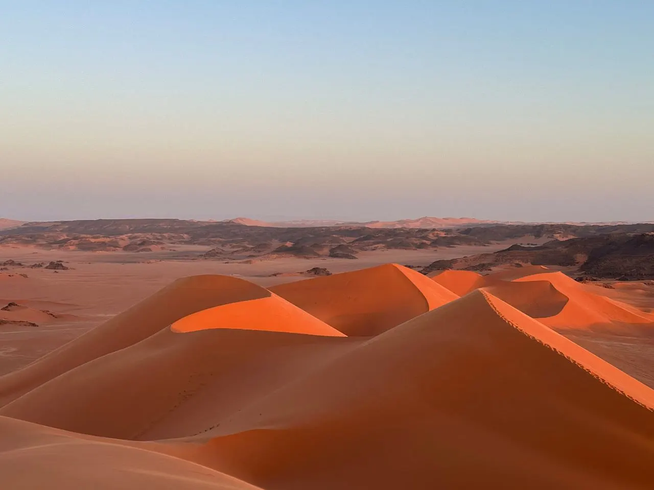 Dunes rouges de la Tadrart au coucher du soleil, plateaux rocheux à l'horizon