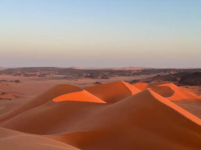 Dunes rouges de la Tadrart au coucher du soleil, plateaux rocheux à l'horizon
