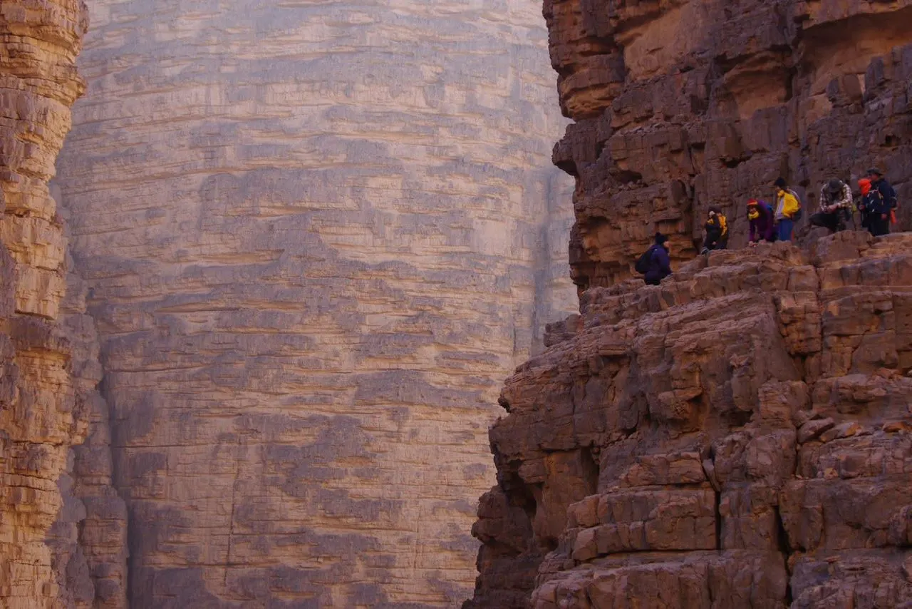 Randonneurs sur une corniche, entre les hautes parois d'un canyon du Tassili